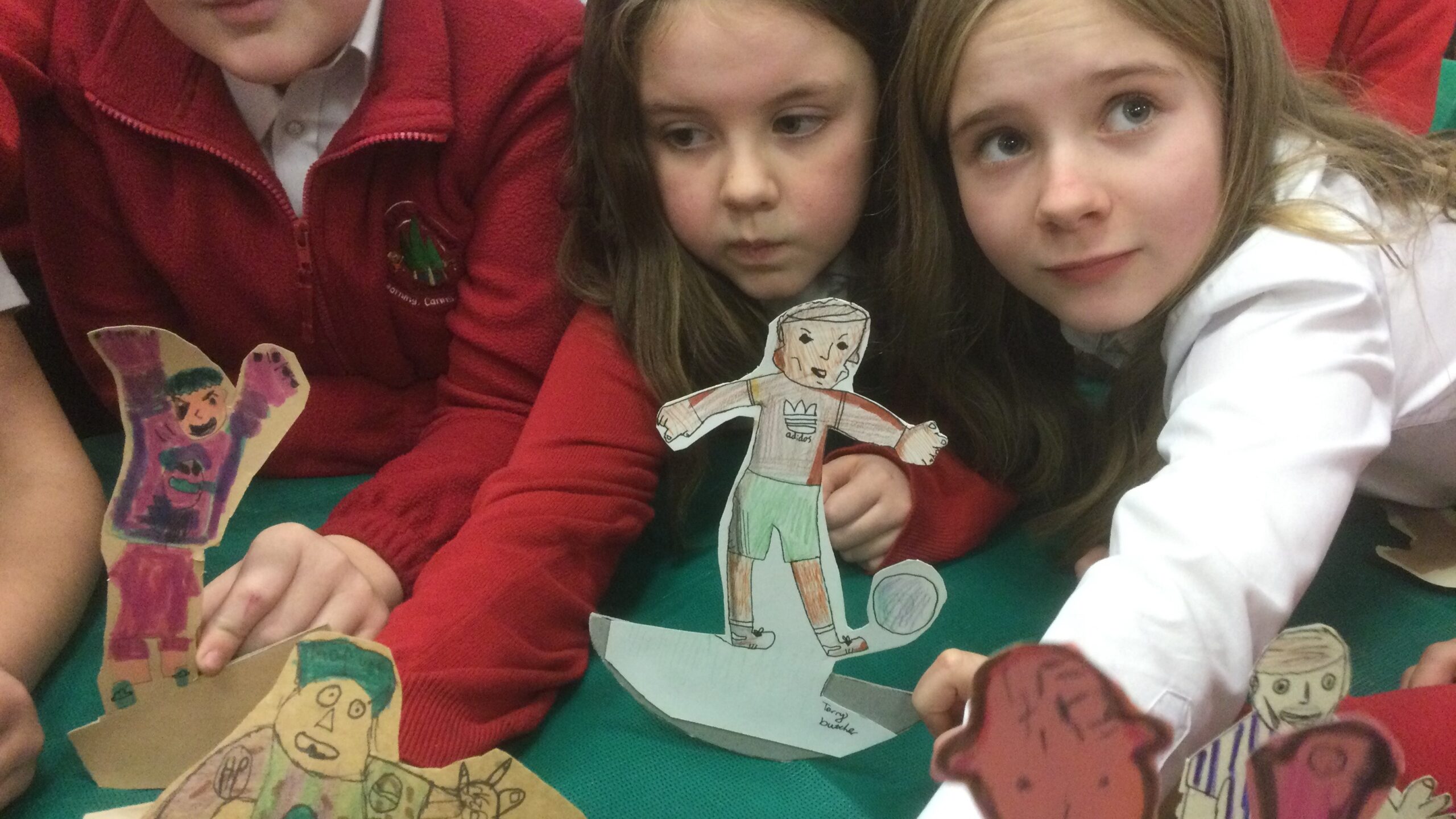 A child looks up at the camera, whilst other children around her hold out cardboard football figures