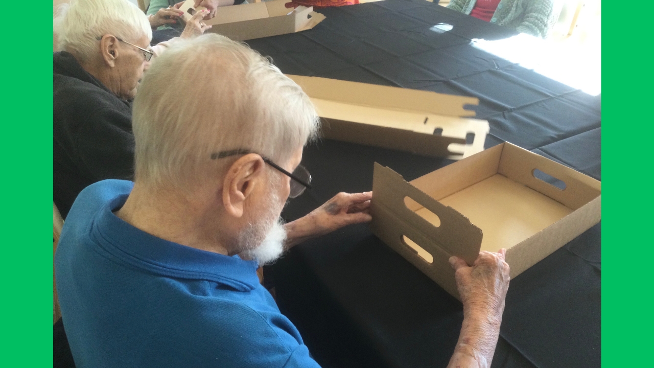 Two gentlemen seated at a table, folding flat pack cardboard boxes into shape