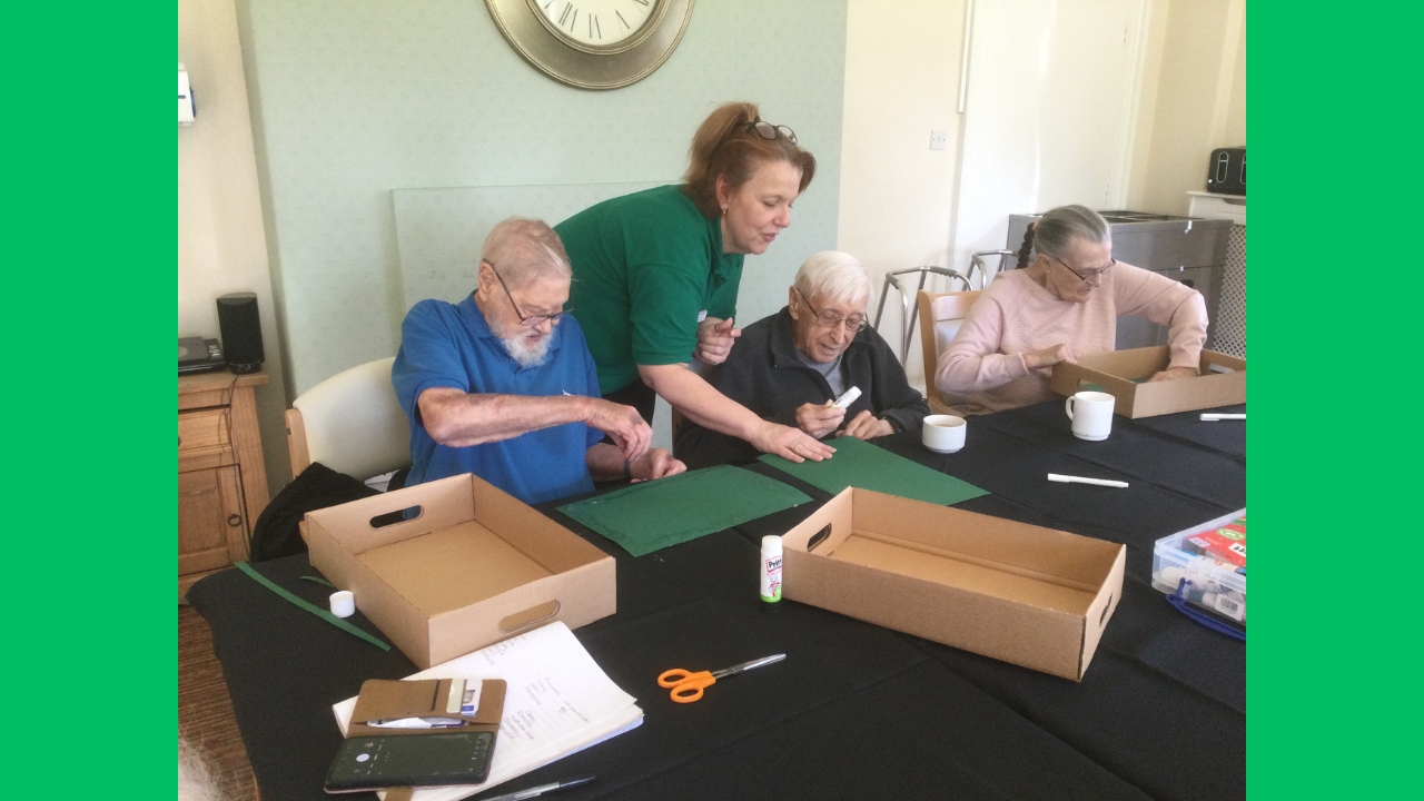 A group of Manor Farm residents working with the Activities Co-ordinator to stick green paper inside shallow cardboard boxes