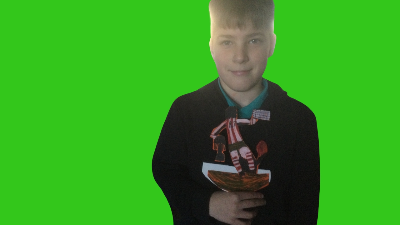 A school child dressed in dark top with green shirt collar showing, holding a football figure coloured in red and black