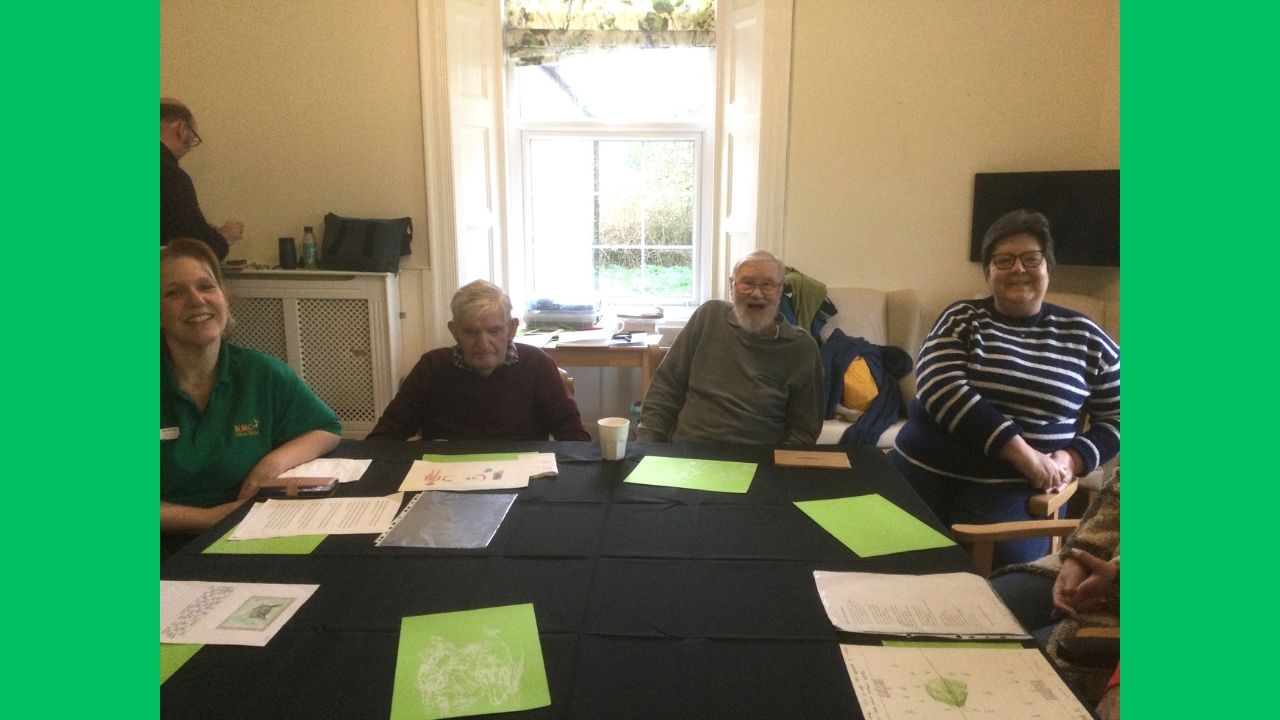 A group of four people seated around a table covered in black cloth with green papers strewn across the top