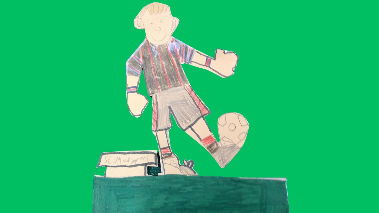 A cut-out football figure in black and red stripe and balancing football on his foot with the name St Margarets written beside him