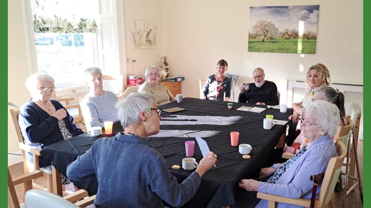 A group of people around a table, with beakers and cups in front of them, discussing a picture