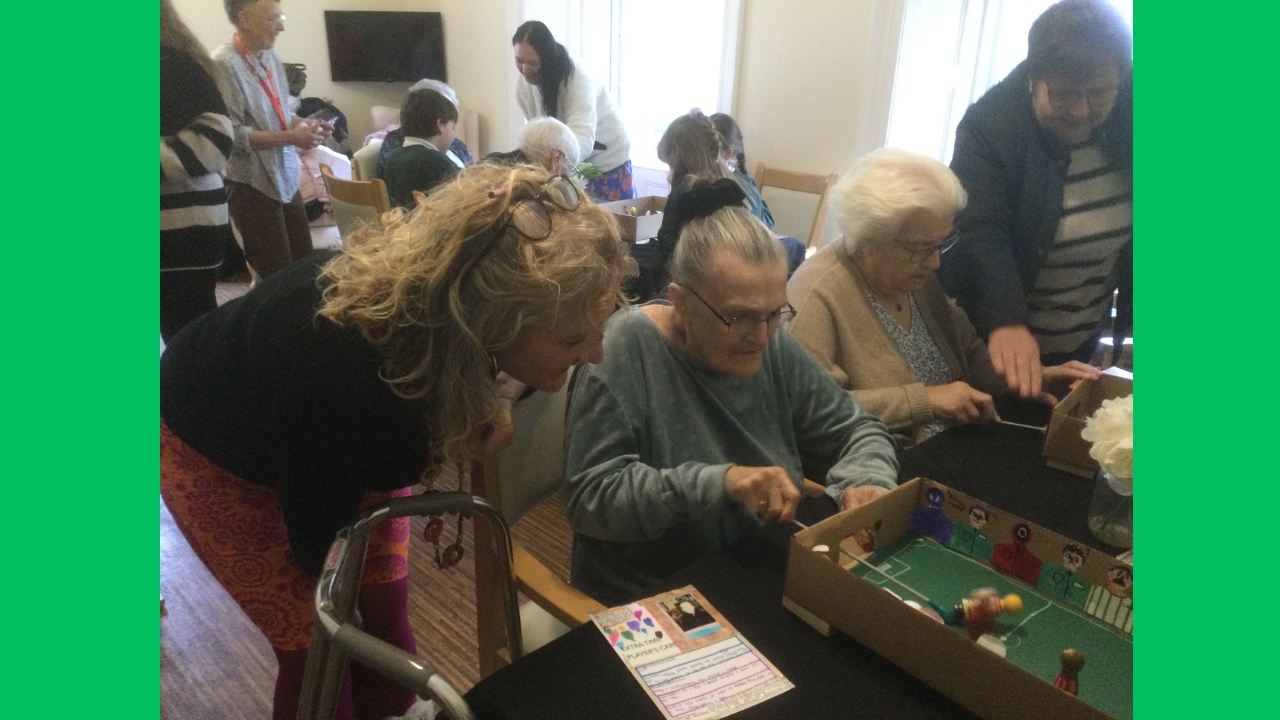 A room full of people some seated some standing all intent upon watching or playing table top magnetic football