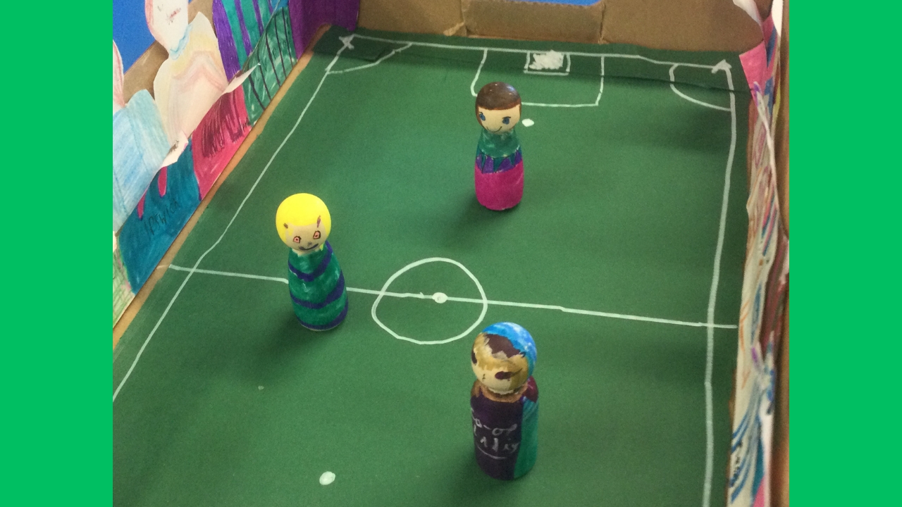 Three brightly coloured wooden figures on a handmade football pitch