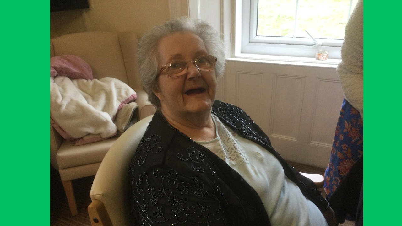 A woman wearing spectacles and dressed in a grey top with a black sparkly jumper grins at the camera