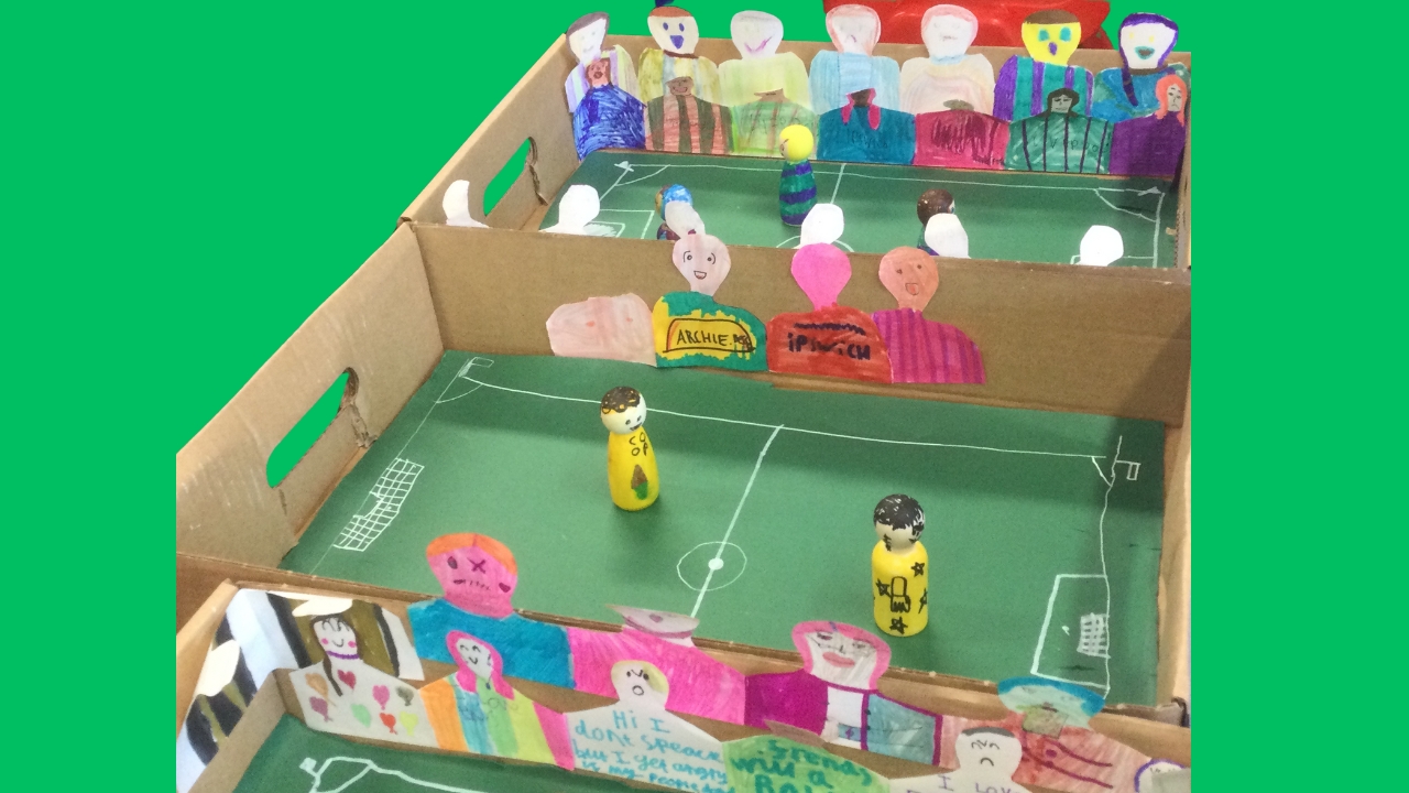 Two cardboard football pitches with hand coloured supporters glued to the sides and wooden figures as players