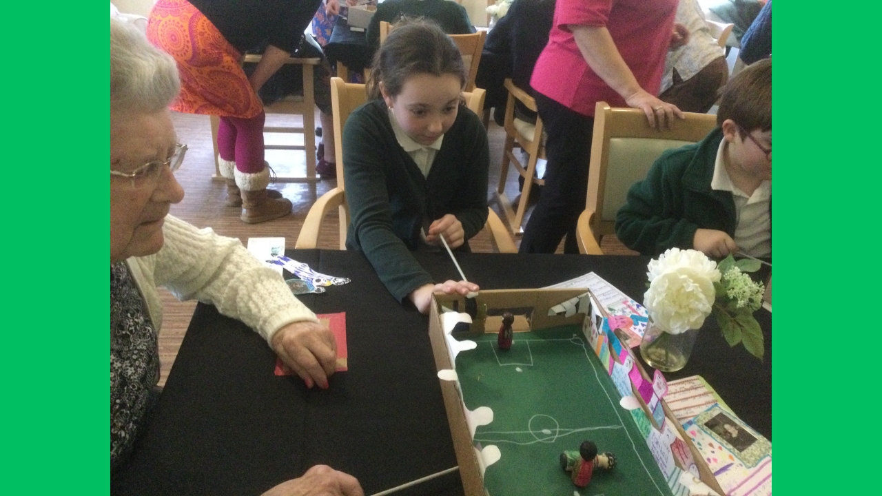 A child focuses intently on her wooden player as she tries to score a goal in her game of magnetic football whilst a resident tries to block her kick