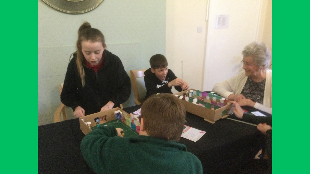 Children and adults seated at a table with cardboard box football pitches in front of them playing a game of football