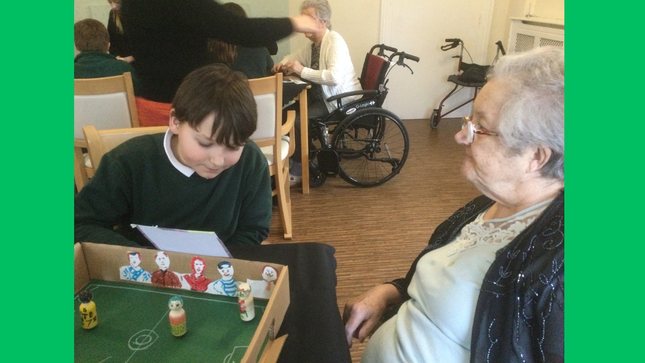 A child sits beside a resident, reading from a card he's holding. In front of them is a hand made football game