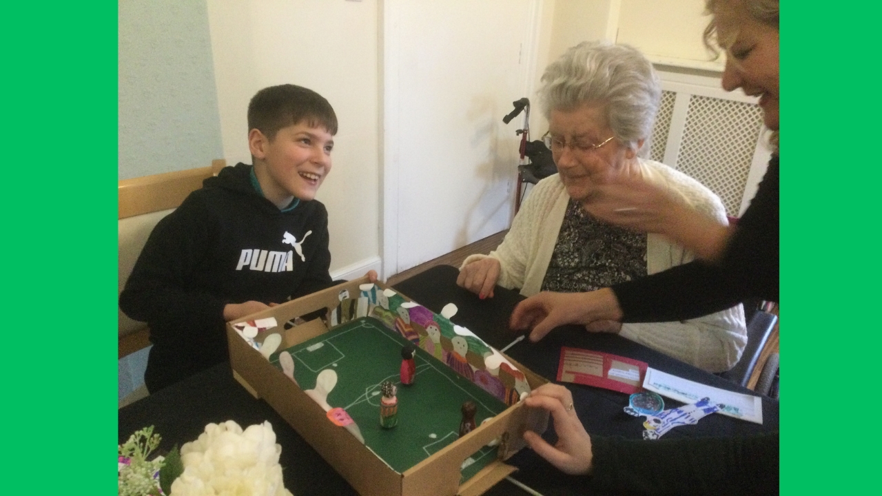 A boy laughs as two women, one seated, one standing attend to a magnetic football game on the table in front of them