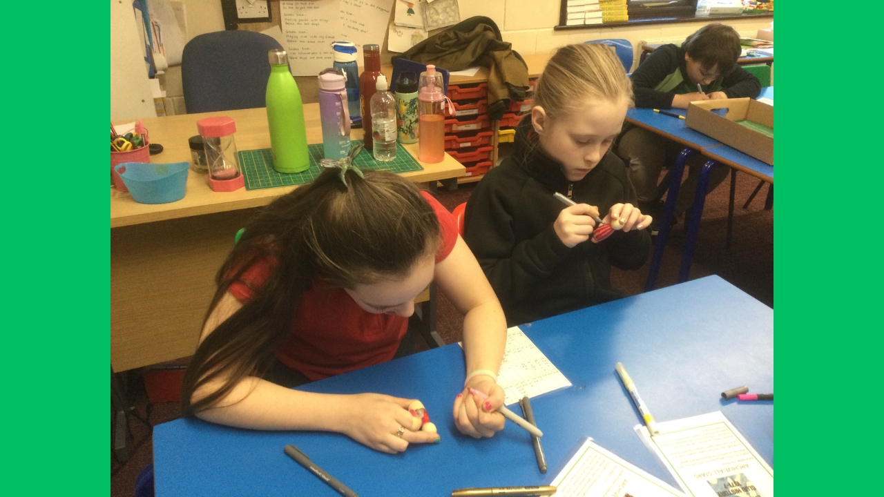 Two school girls concentrated on colouring their wooden figures