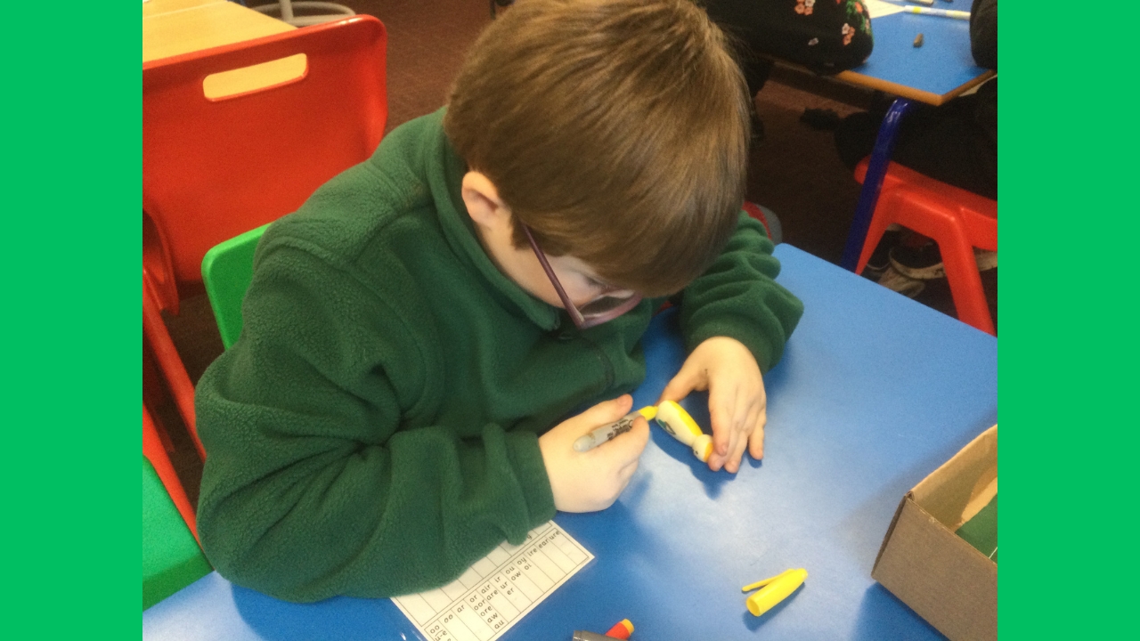 A school boy uses a yellow felt tip pen to colour a small wooden figure